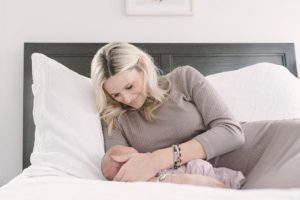 mom lays with baby girl on bed at home