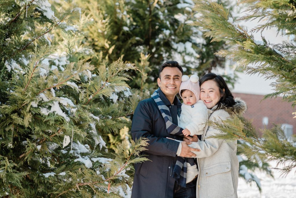 family cuddles in pine trees during snowy Nashville family portraits