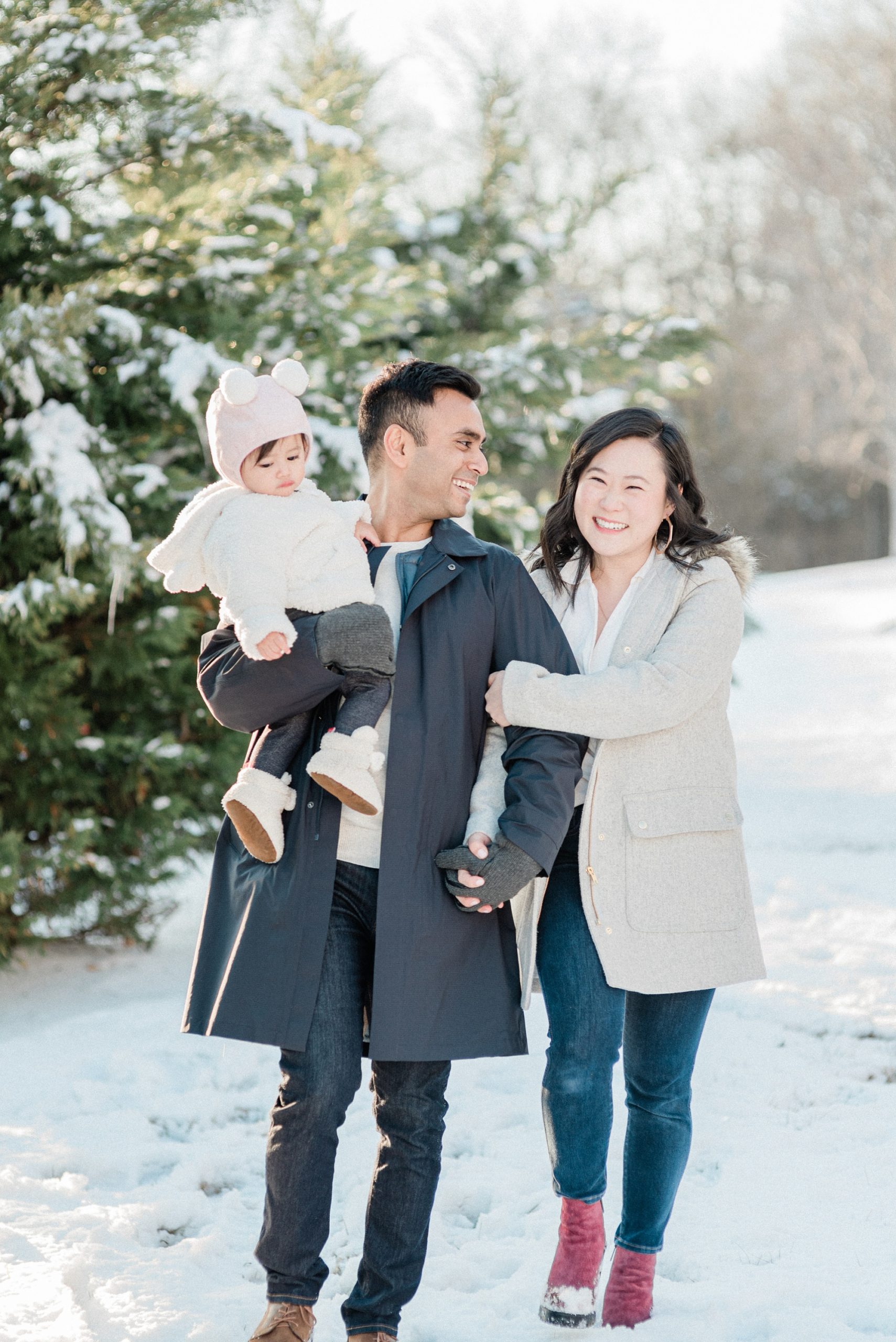 husband and wife hold hands walking with daughter during snowy Nashville family portraits
