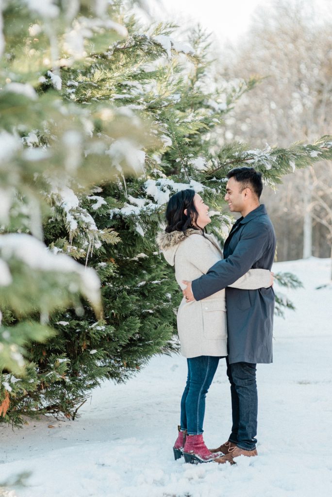 married couple hugs by trees during snowy Nashville family portraits