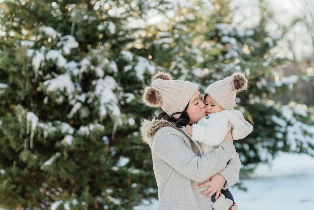 mom kisses daughter in matching hat during session in the snow