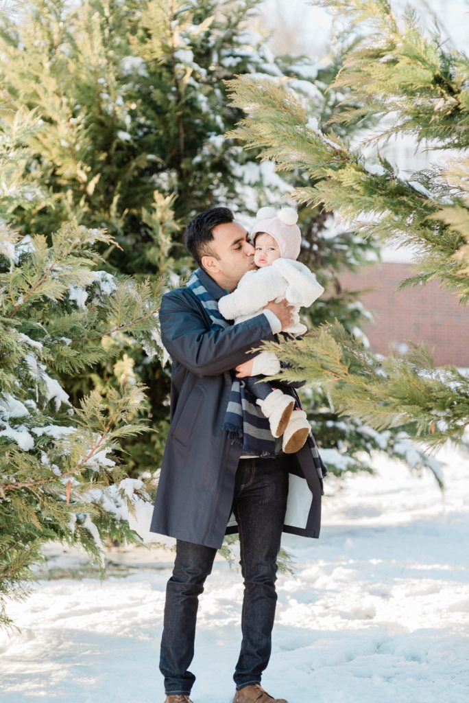 dad hugs and kisses one year old daughter in the snow