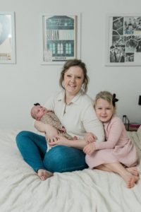 mom and daughters sit on bed during lifestyle newborn photos at home