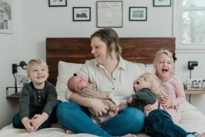 mom sits with four children on bed during Franklin TN newborn portraits at home