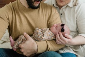 parents look down at newborn girl in burgundy bow during Franklin TN newborn portraits at home