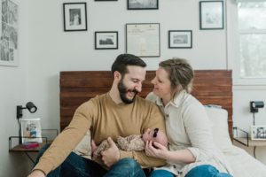 parents laugh looking at each other with baby girl in arms