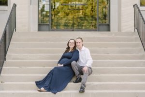 pregnant woman in blue dress sits on steps at Vanderbilt University with husband
