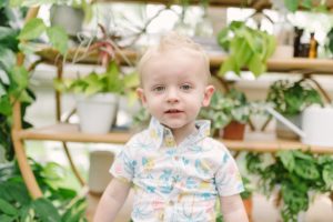 toddler in beach shirt poses by wall of plants at East Nashville Greenhouse