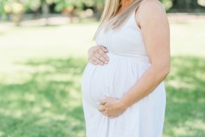 mom in white dress holds belly during maternity photos in Nashville TN