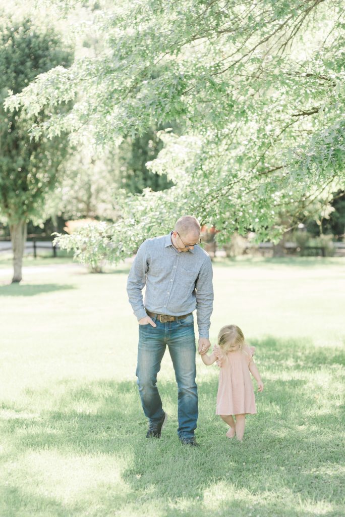 dad holds daughter's hand walking through yard