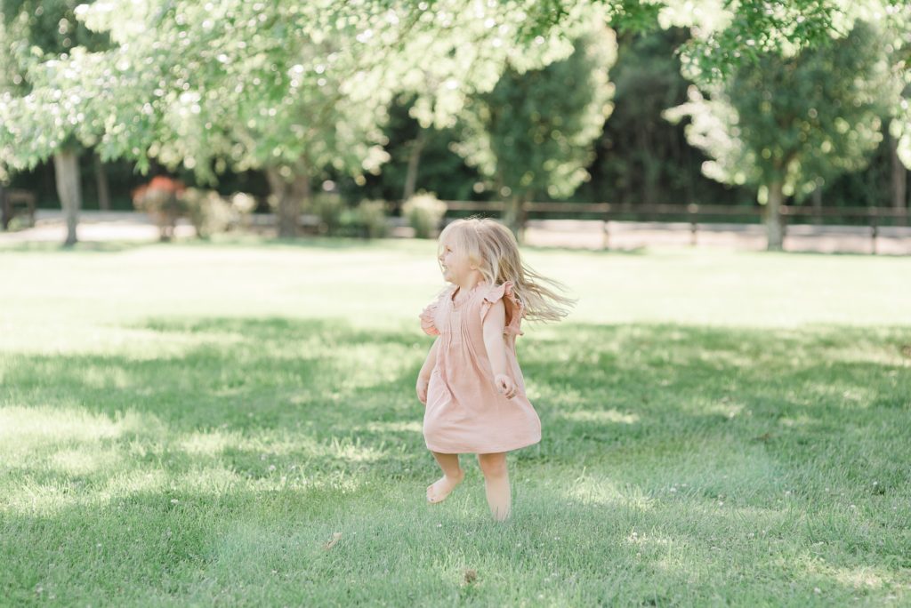 toddler in pink dress dances during backyard family photos