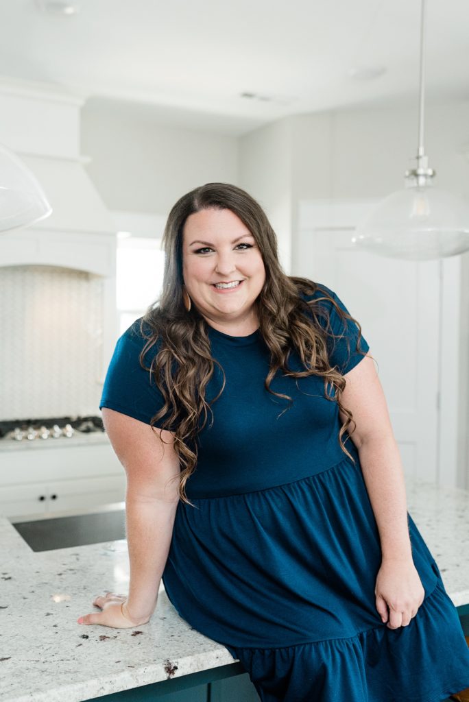 business owner in navy dress sits on kitchen counter