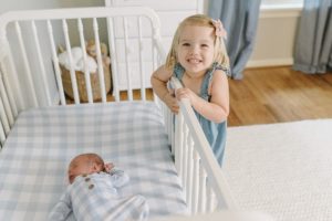 big sister looks over crib at baby boy