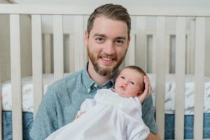dad holds baby girl against crib at home