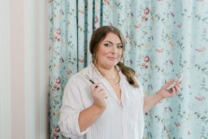 woman holds makeup brushes by floral curtain at the Nashville Graduate Hotel