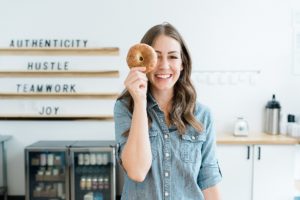 woman holds bagel up to eye in kitchen during branding photos