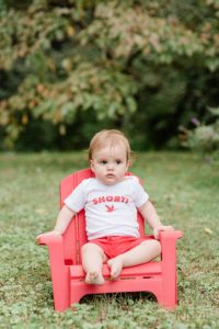 toddler sits in red chair during family photos