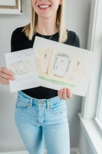 woman holds up watercolor paintings