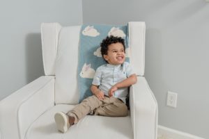 toddler sits in nursery chair during newborn photos at home