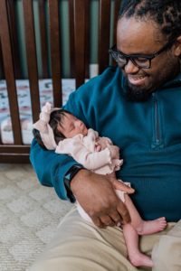 dad holds daughter sitting by crib during Nashville lifestyle newborn session