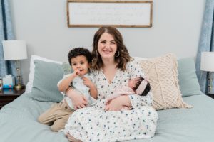 mom sits holding two children on bed during newborn photos at home