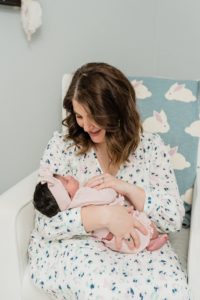 mom looks down at baby girl during newborn photos at home