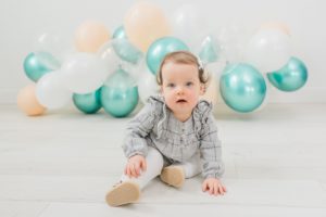 toddler smiles playing by balloon garland during studio milestones photos