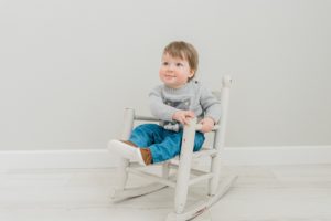 baby sits in rocking chair during studio first birthday photos