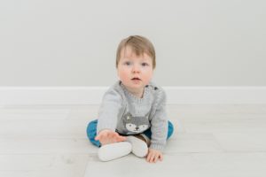 baby sits on floor in studio playing with feet