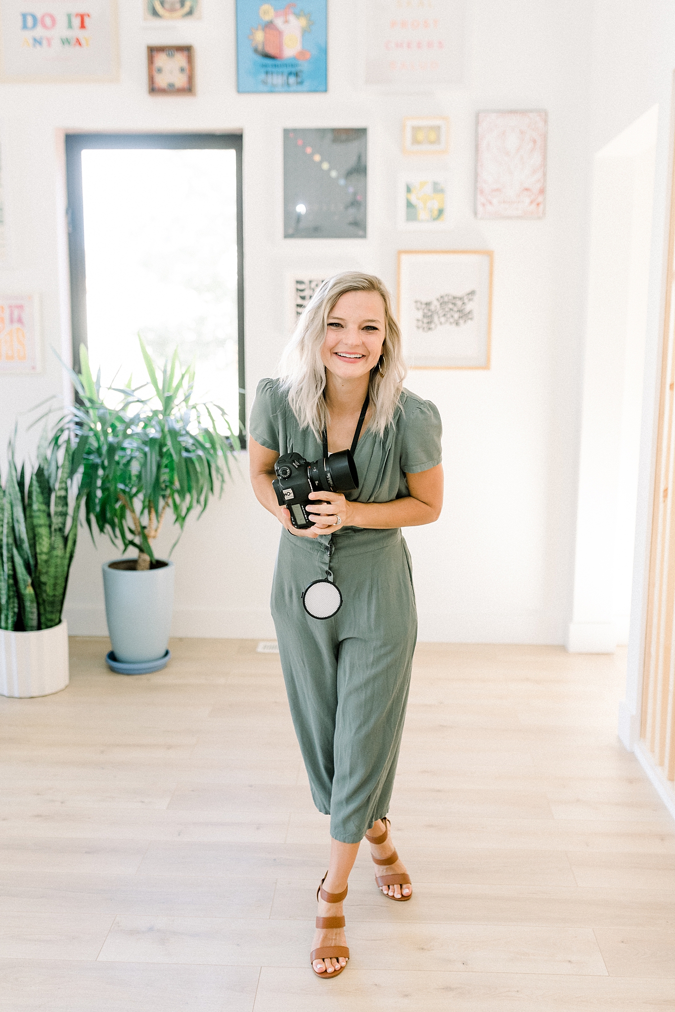 a_wedding_photographer_is_wearing_a_green_jumpsuit_and_is_walking_across_a_studio_holding_a_camera