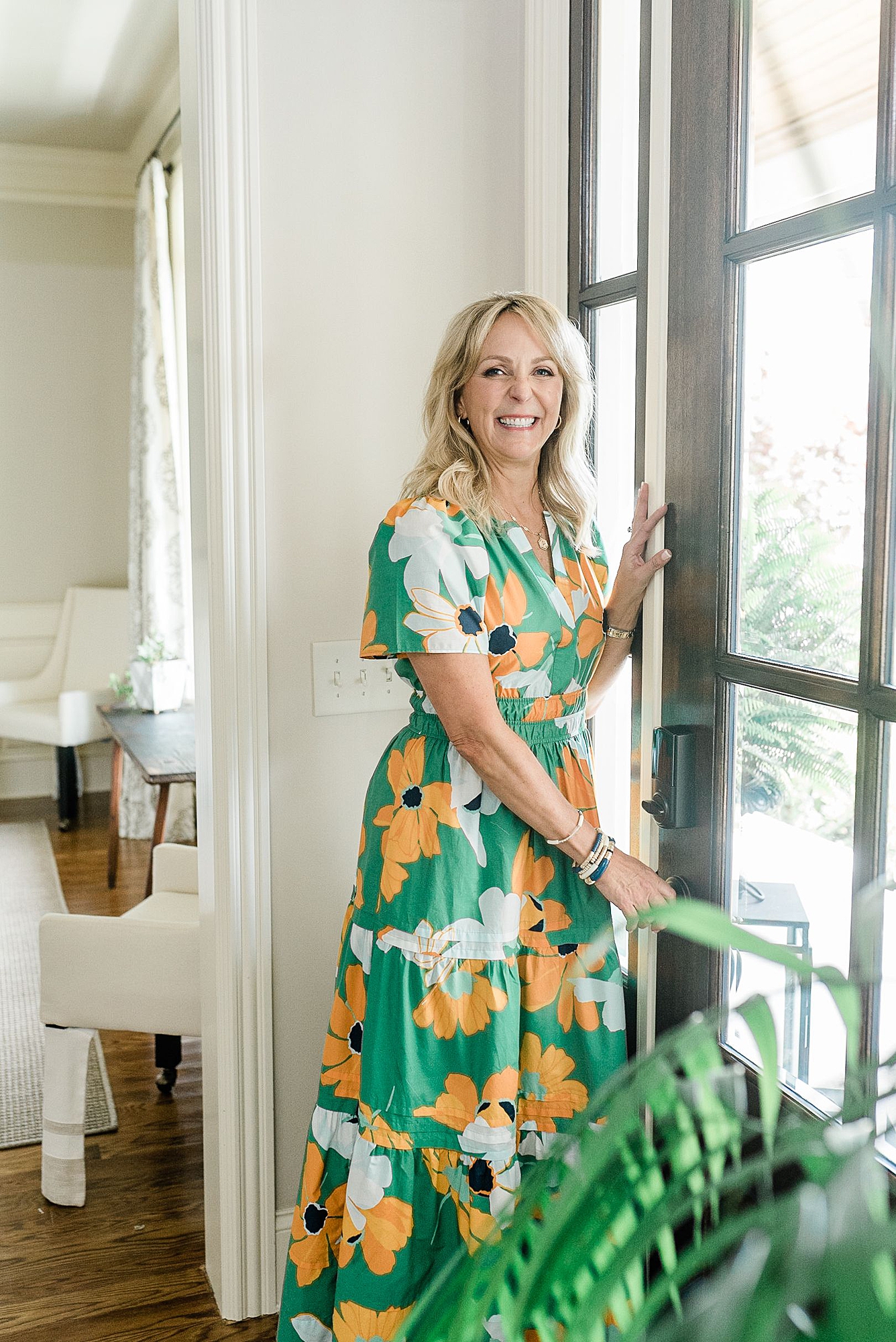 a_nashville_realtor_ashley_hicks_is_wearing_a_green_dress_and_opening_a_door_and_smiling_at_the_camera