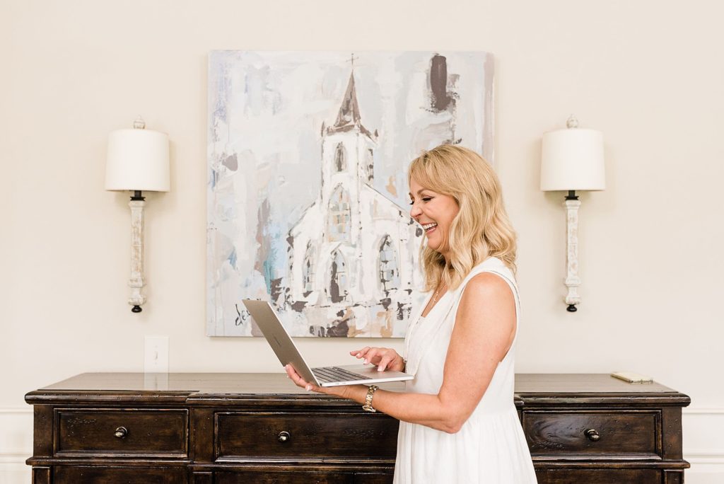 a_middle_aged_woman_is_smiling_and_wearing_a_white_dress_and_standing_while_typing_on_a_computer_branding_photos