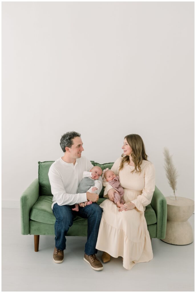 mom_and_dad_are_sitting_on_green_couch_holding_their_newborn_twins_for_holiday_photos_in_studio_with_Nashville_Photographer_Dolly_DeLong_Photography