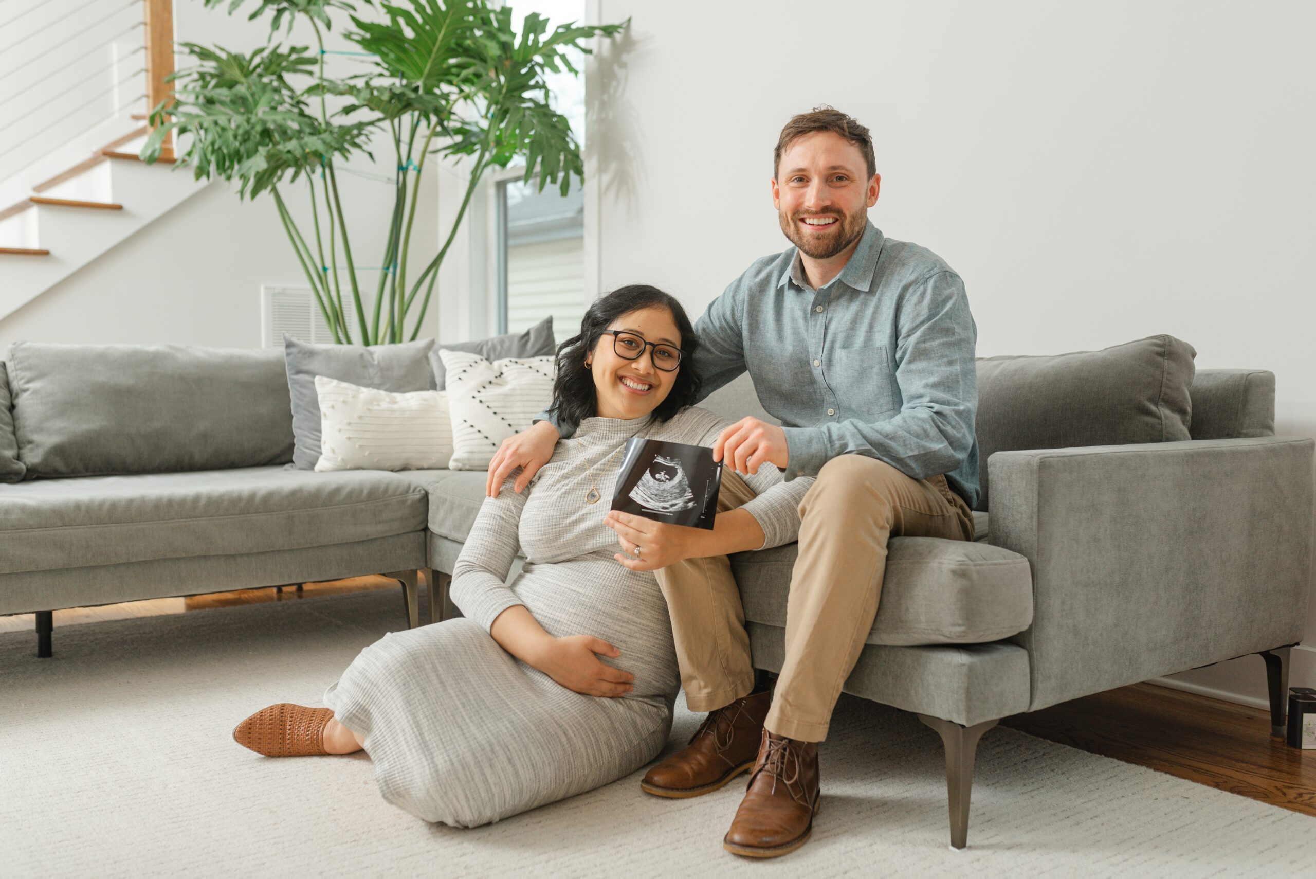 a_husband_and_pregnant_wife_hold_up_ultra_sound_photo_in_their_living_room_for_maternity_photos_with_Nashville_Maternity_photographer_dolly_DeLong_Photography