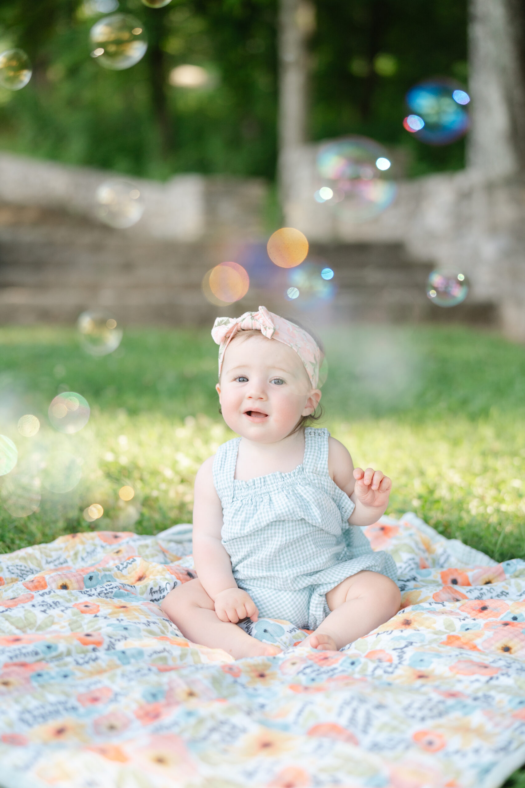 Baby girl sitting on a colorful blanket outdoors surrounded by bubbles — a playful example of baby photography ideas that capture natural joy.