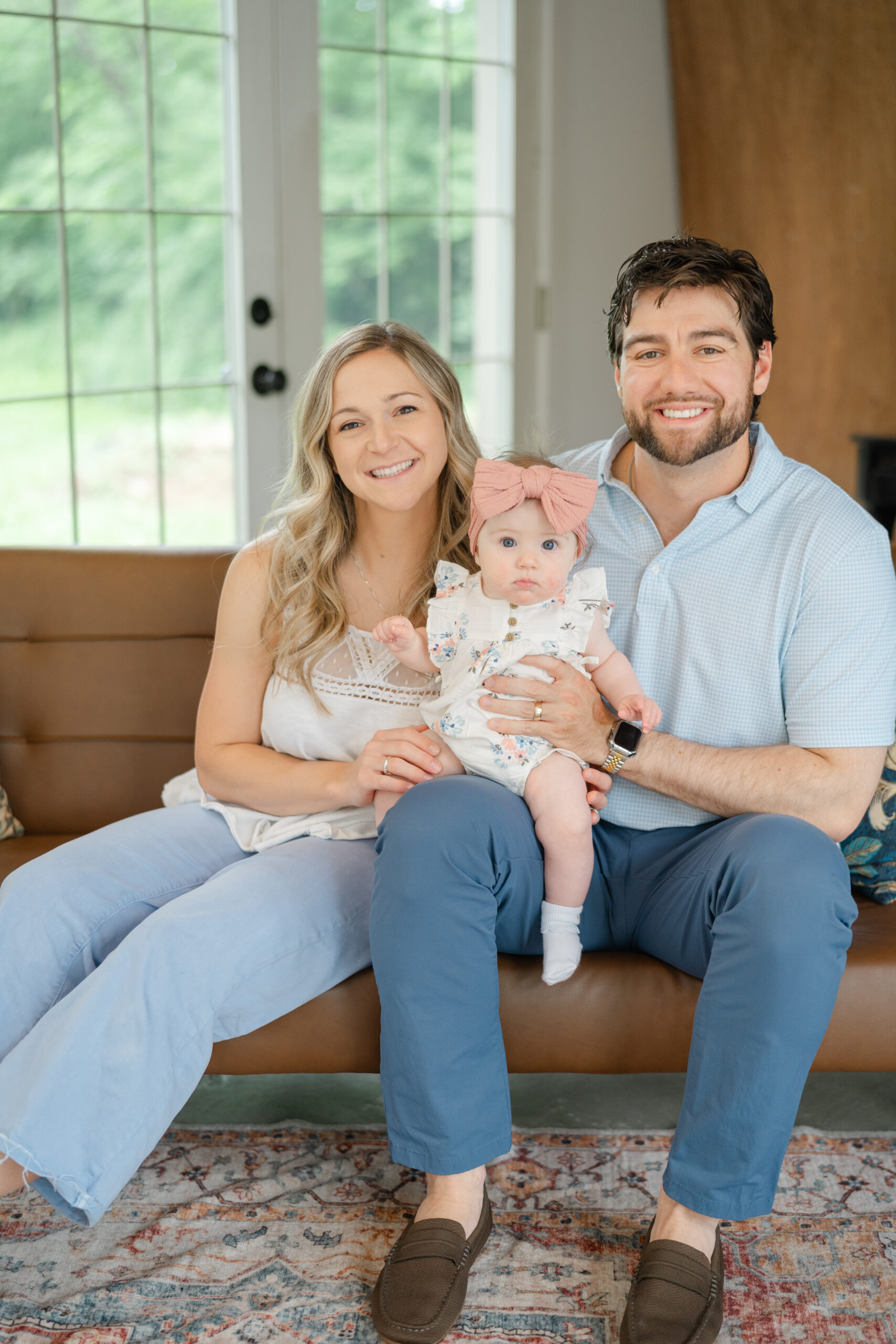 Smiling family sitting on a couch with their baby girl, an example of natural light baby photography ideas for at-home sessions.