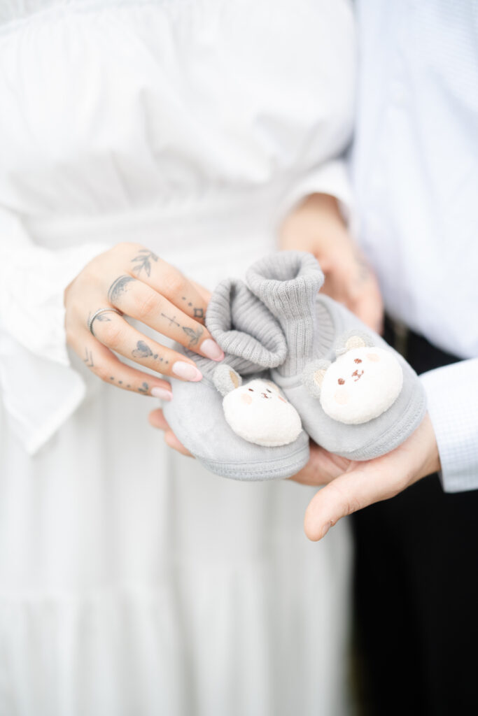 Couple holding a pair of soft gray baby booties during a maternity session, symbolizing anticipation and love. what to wear for maternity photos