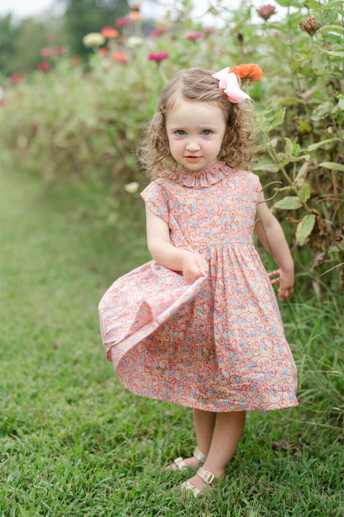 Little girl twirling in a field of flowers, holding her dress and making eye contact with the camera, a classic child lifestyle portrait. family photography poses.