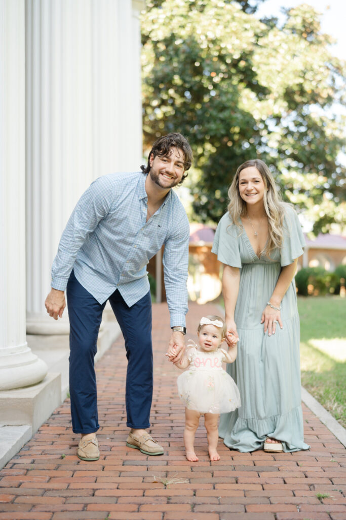 Family walking together holding hands as their baby stands between them during her one-year milestone session.