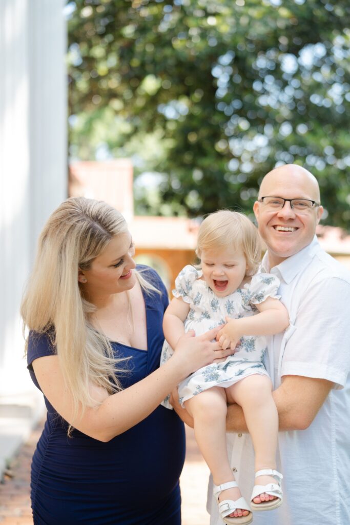 a family is tickling their toddler while holding her at their maternity session at the nashville ellington ag center with maternity photographer dolly delong