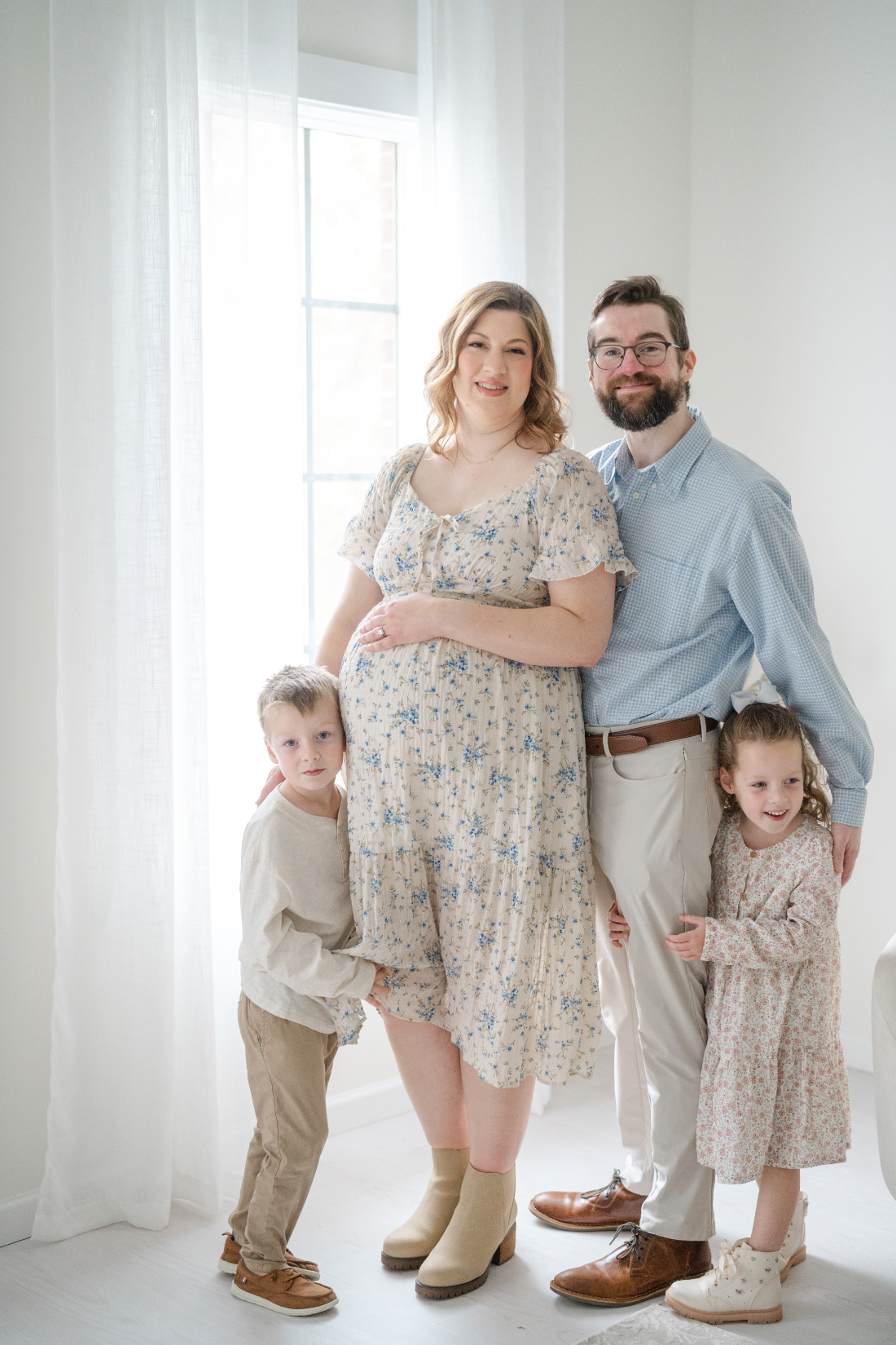 Franklin TN photographer captures a family of four standing together near a bright window in a minimal studio space.
