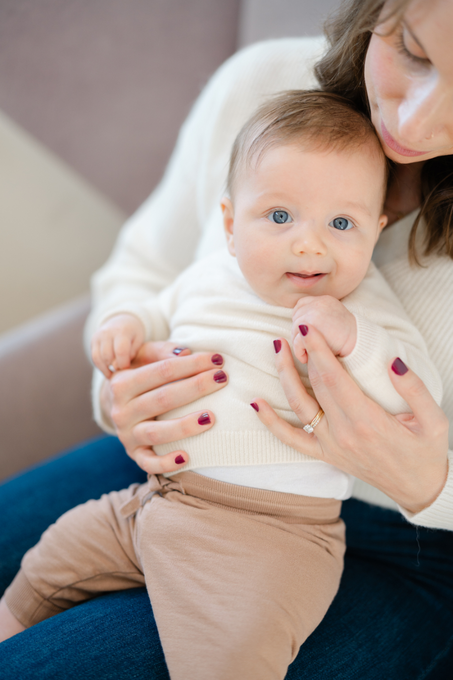 Smiling baby with bright blue eyes sitting on mother’s lap during a baby milestone photoshoot 