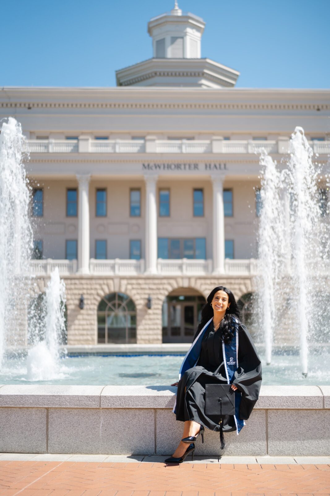 College graduation photos at Belmont University featuring a grad in cap and gown at the McWhorter Hall and freedom fountain in Nashville