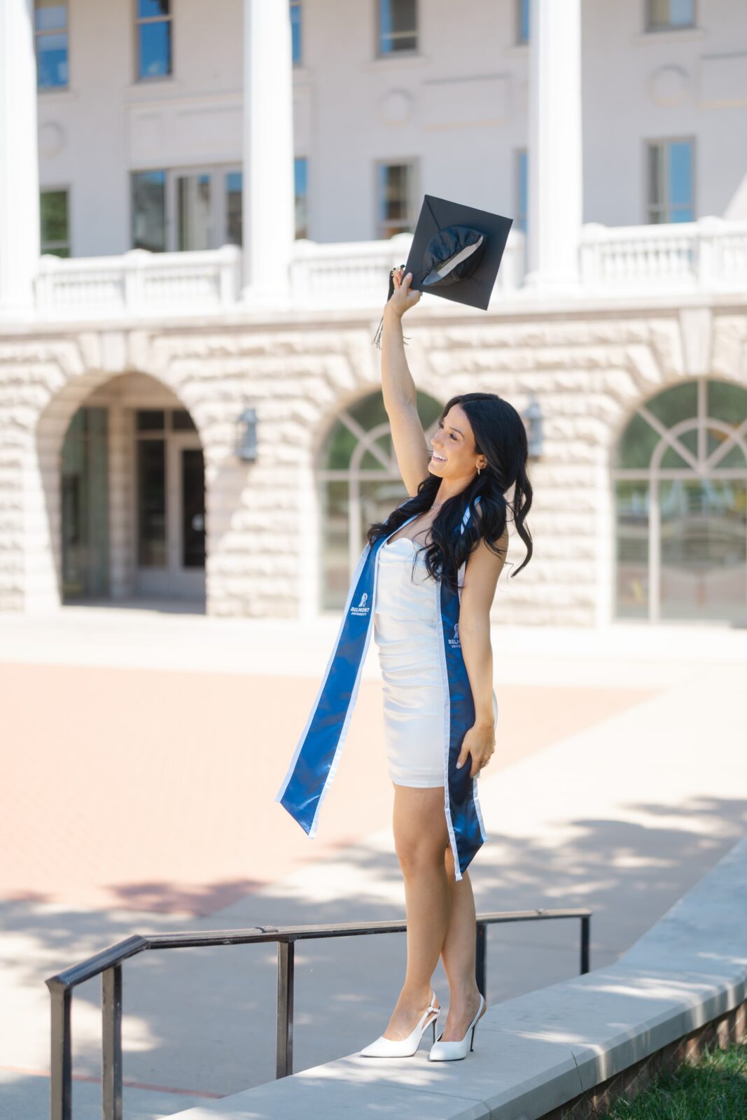 Joyful college graduation photo at Belmont University with a grad lifting her cap outside McWhorter Hall in Nashville TN