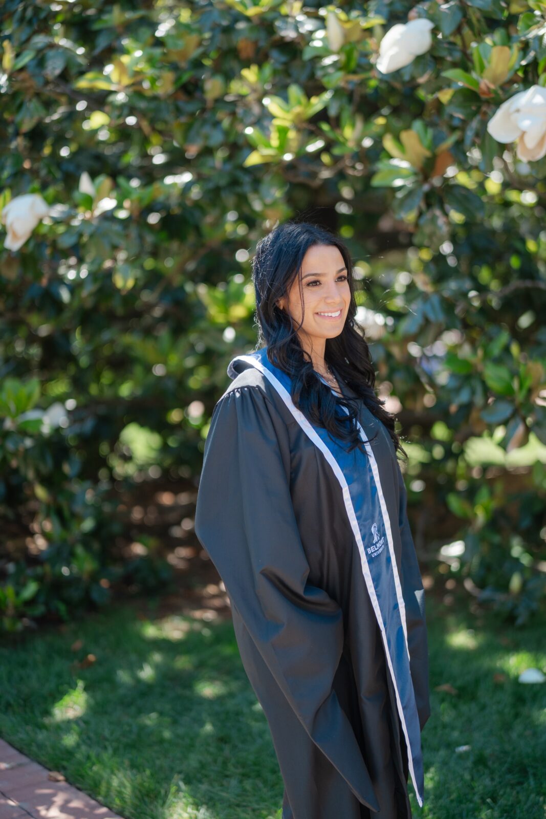 Graduation portrait at Belmont University with a smiling grad in her gown beside a blooming magnolia tree in Nashville