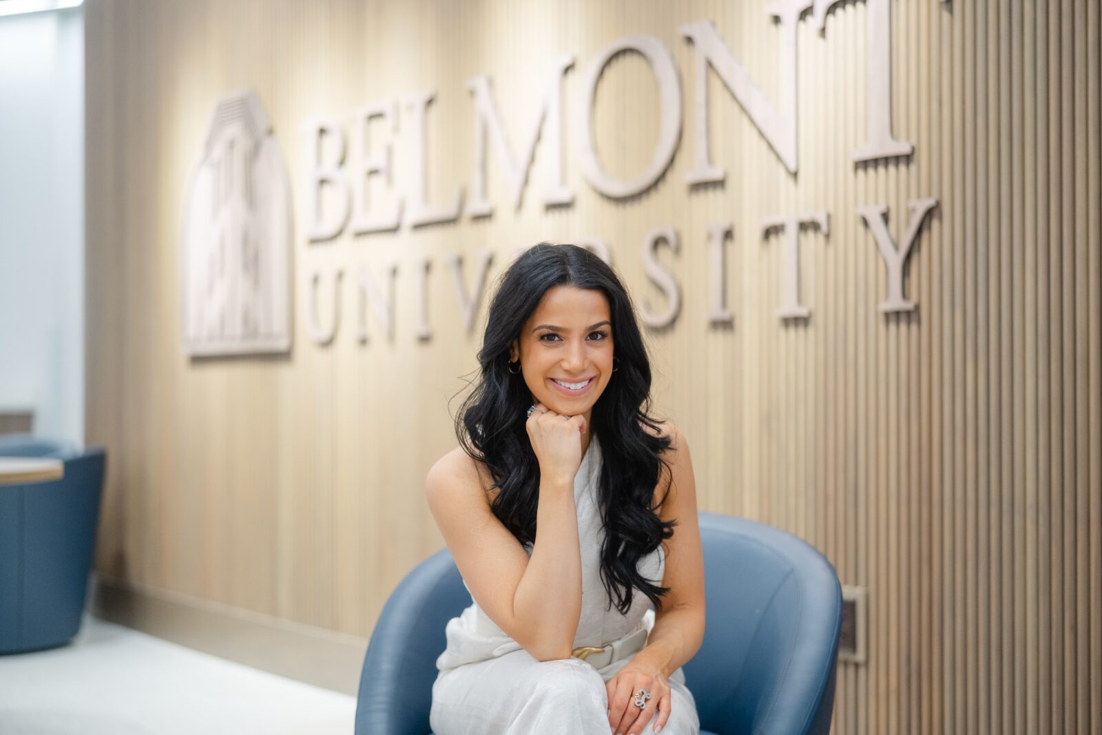 Indoor college graduation portrait at Belmont University with a grad posed in front of the campus lobby sign in Nashville TN