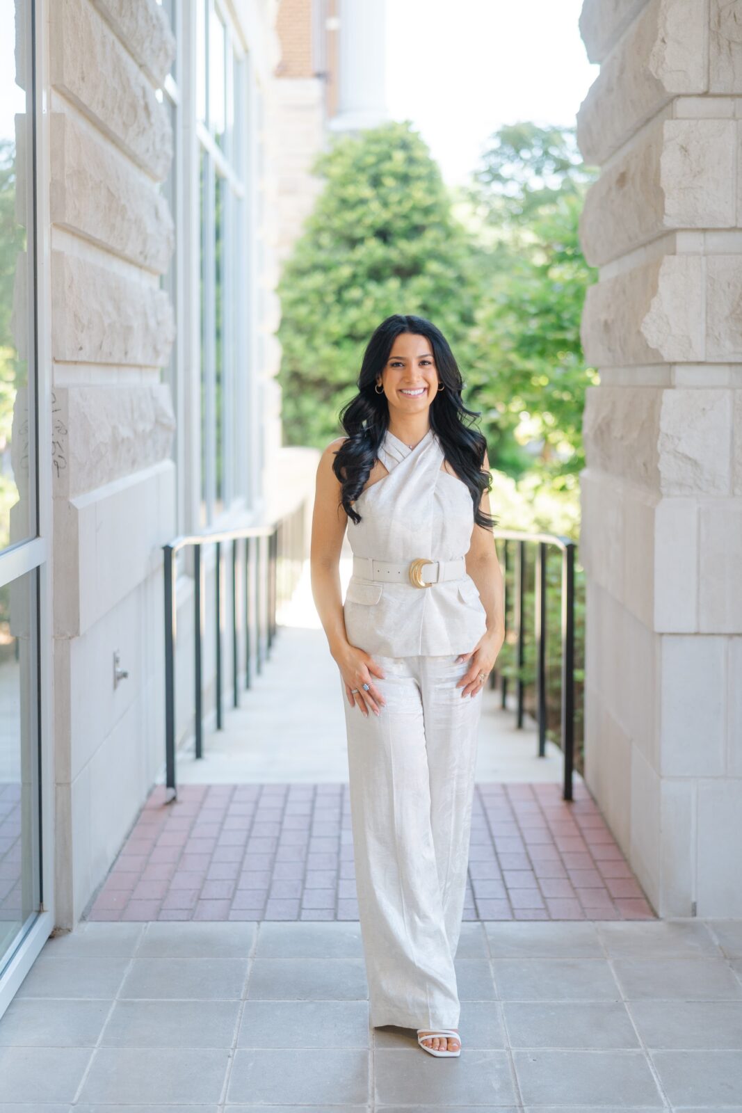 Full-length college graduation photo at Belmont University with a grad in a white outfit framed by stone columns in Nashville TN