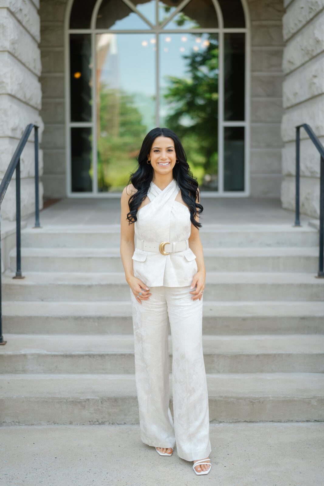 College graduation portrait at Belmont University with a grad in a white outfit on the steps of a stone campus building in Nashville