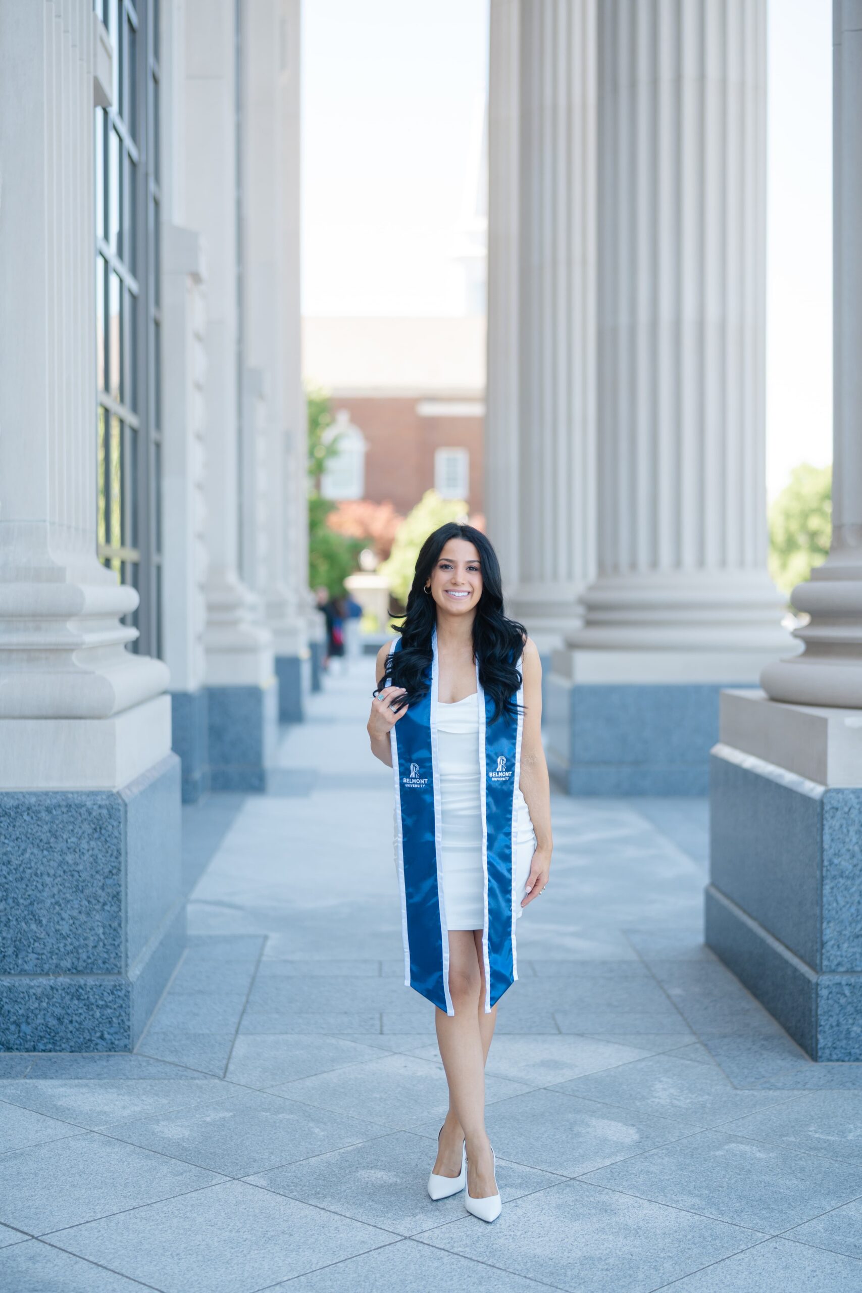 College graduation photos at Belmont University Nashville with graduate in white dress walking through Fisher Center columns