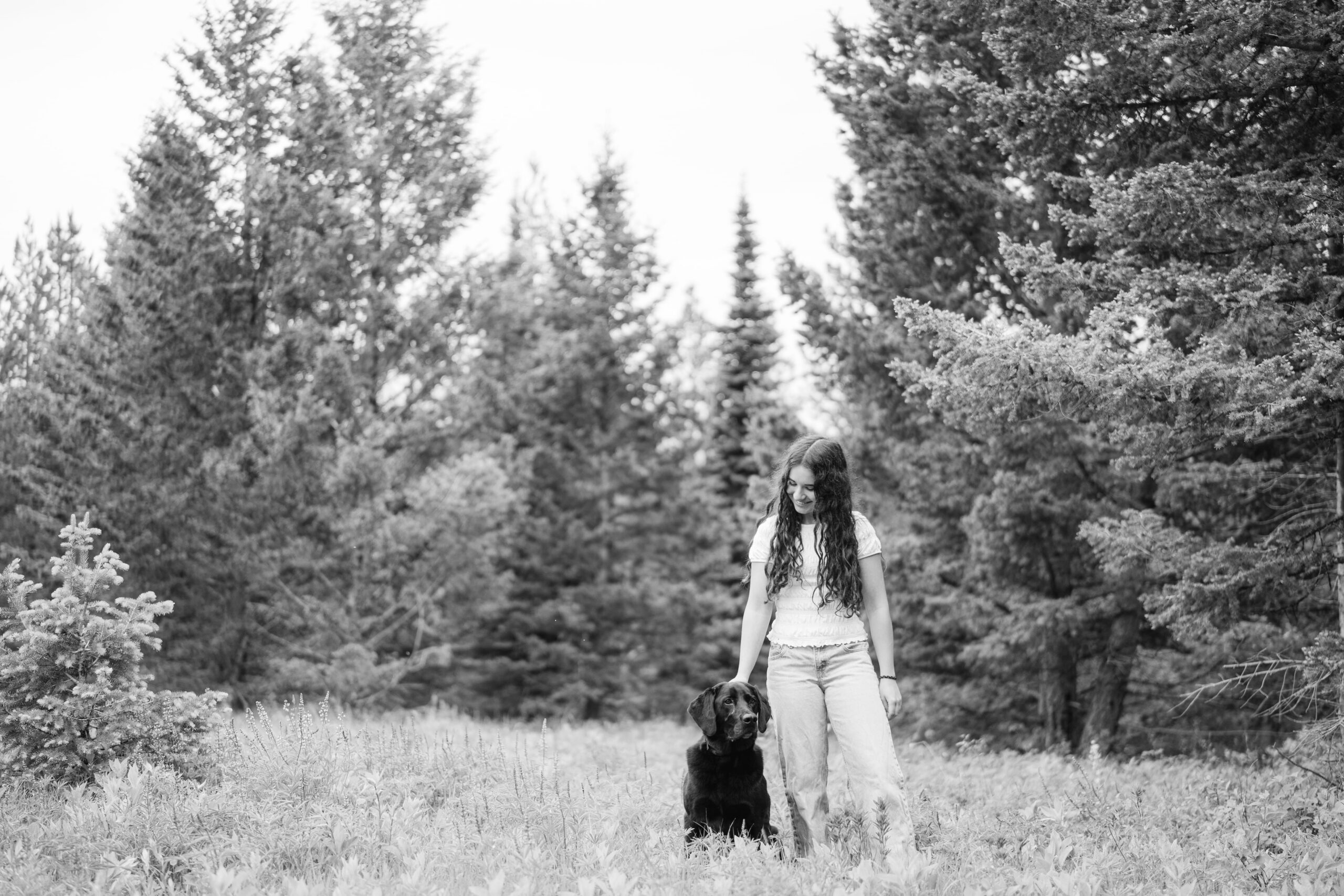 A black and white senior portrait featuring Hayven and her family dog Jet on a Montana hillside.